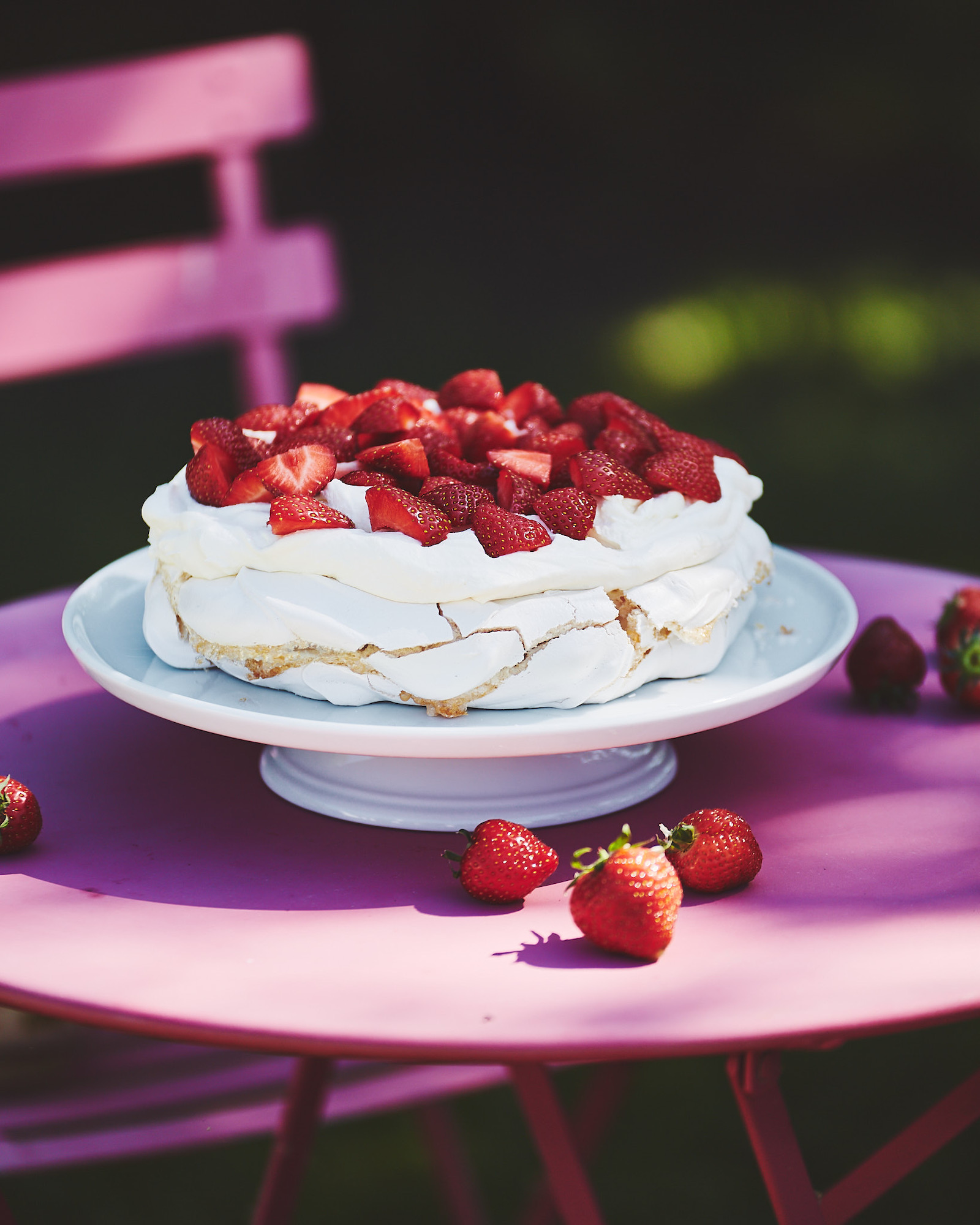 A picture of a pavlova with strawberries sitting on top of a pink table.